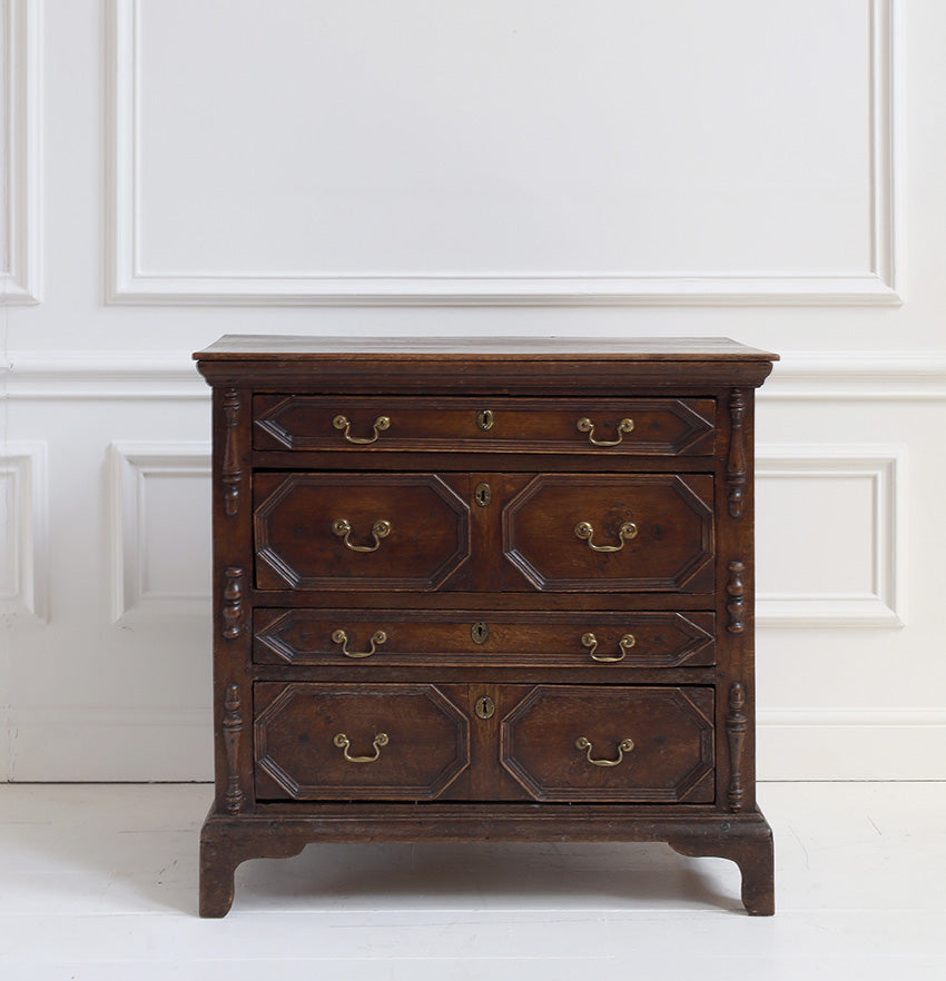 Wooden dresser with four drawers against a white paneled wall