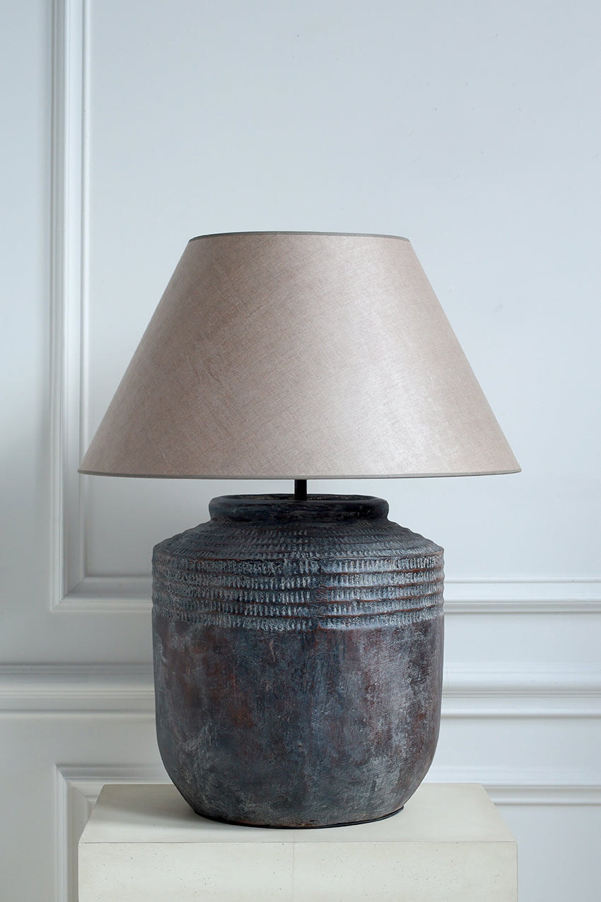 Table lamp with textured base and beige shade on a white surface against a light gray wall.