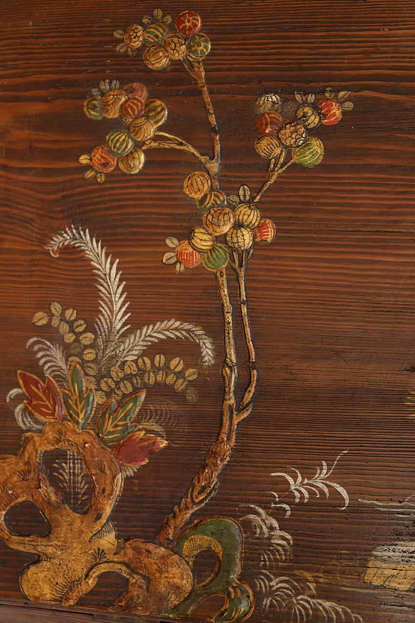 Close-up of a dark brown wooden surface with hand-painted botanical motifs, including branches, acorns, leaves, and decorative scrollwork in muted gold, green, orange, and white tones.