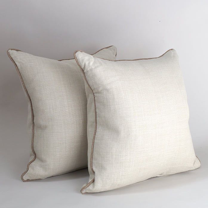 Two square off-white linen throw pillows with beige piping, arranged against a neutral light gray background.