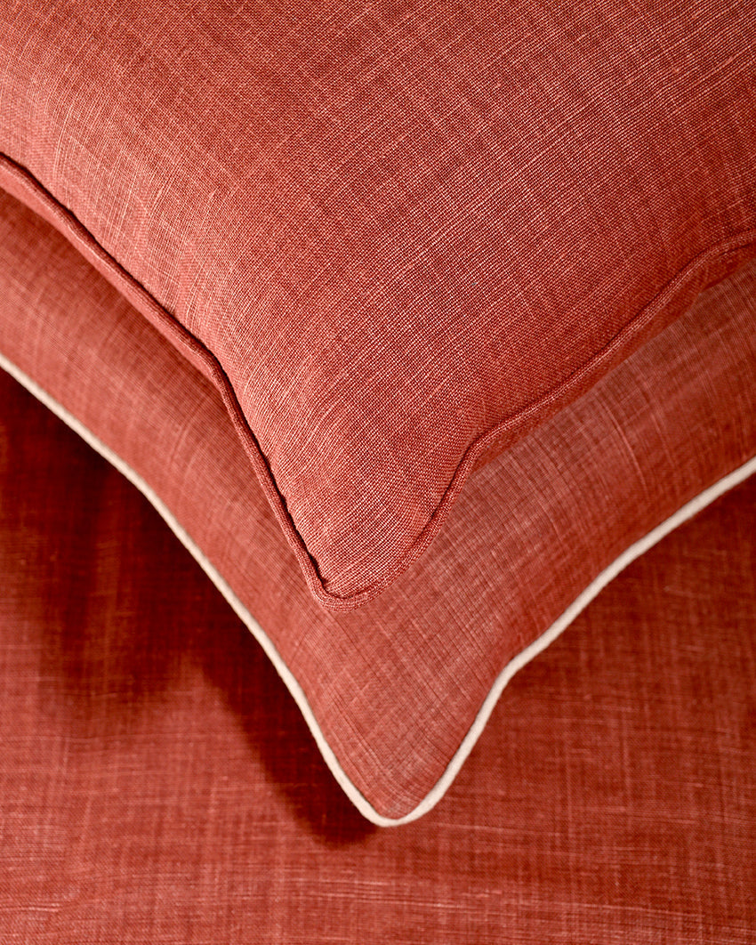 Close-up of a textured rust-orange pillow with a white piped edge resting on matching rust-orange bedding.