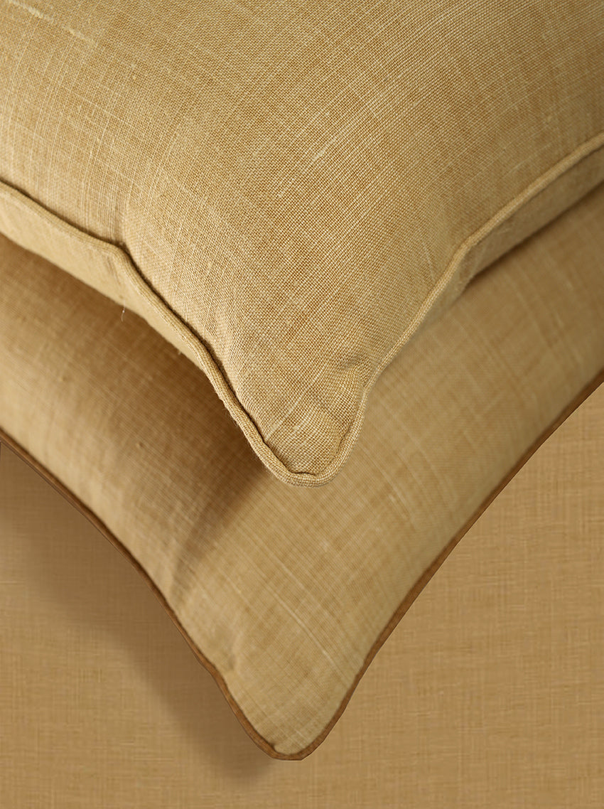 Close-up of two beige textured throw pillows stacked on a matching beige fabric surface, showing the woven fabric detail and stitched edges.