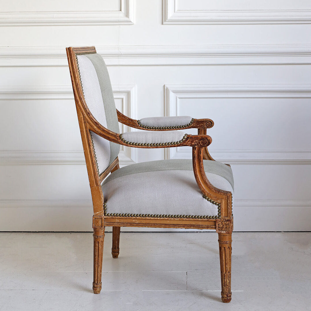 Vintage-style chair with wooden frame and light gray cushion against a white paneled wall.