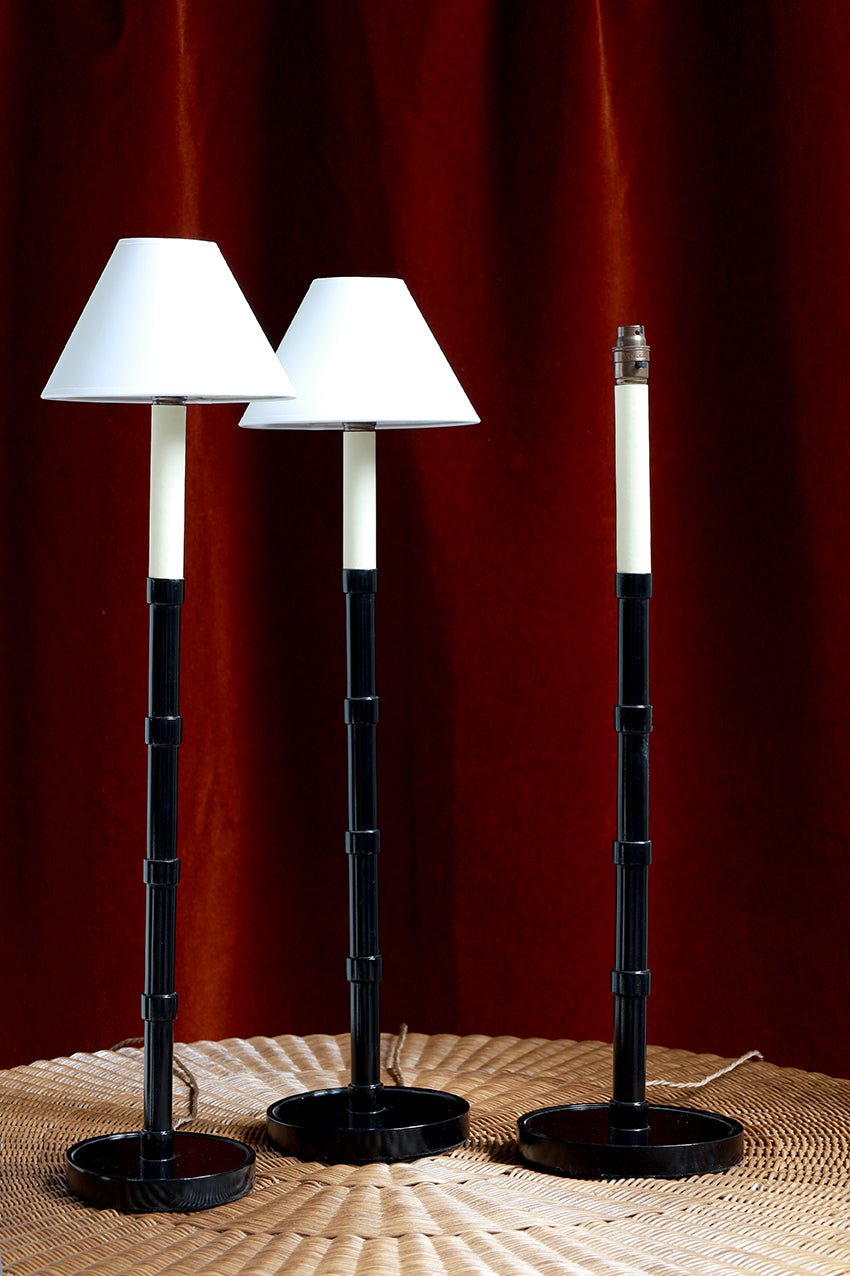 Three black and white lamps on a textured surface with a red curtain background