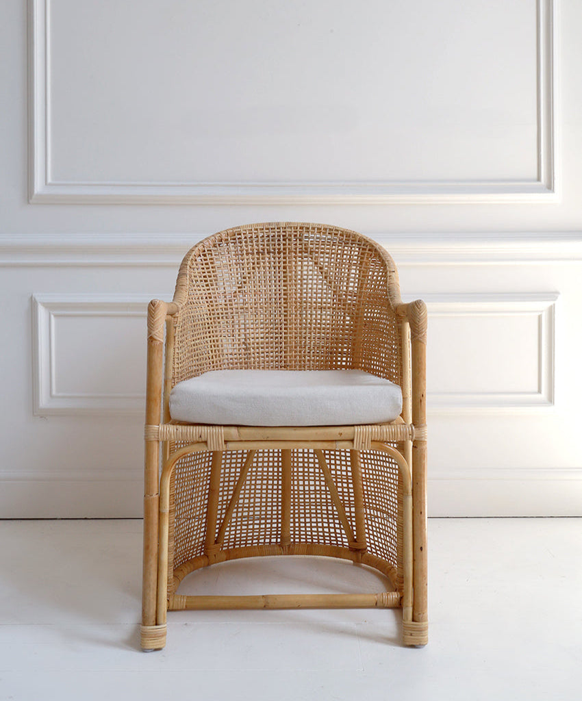 Woven chair with a white cushion against a light-colored wall.
