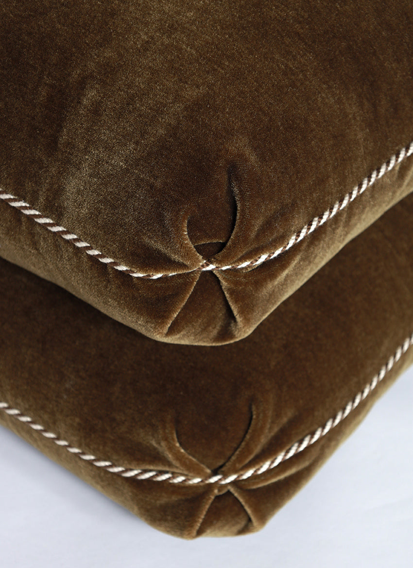 Close-up of a brown velvet pillow with white stitching on a white background