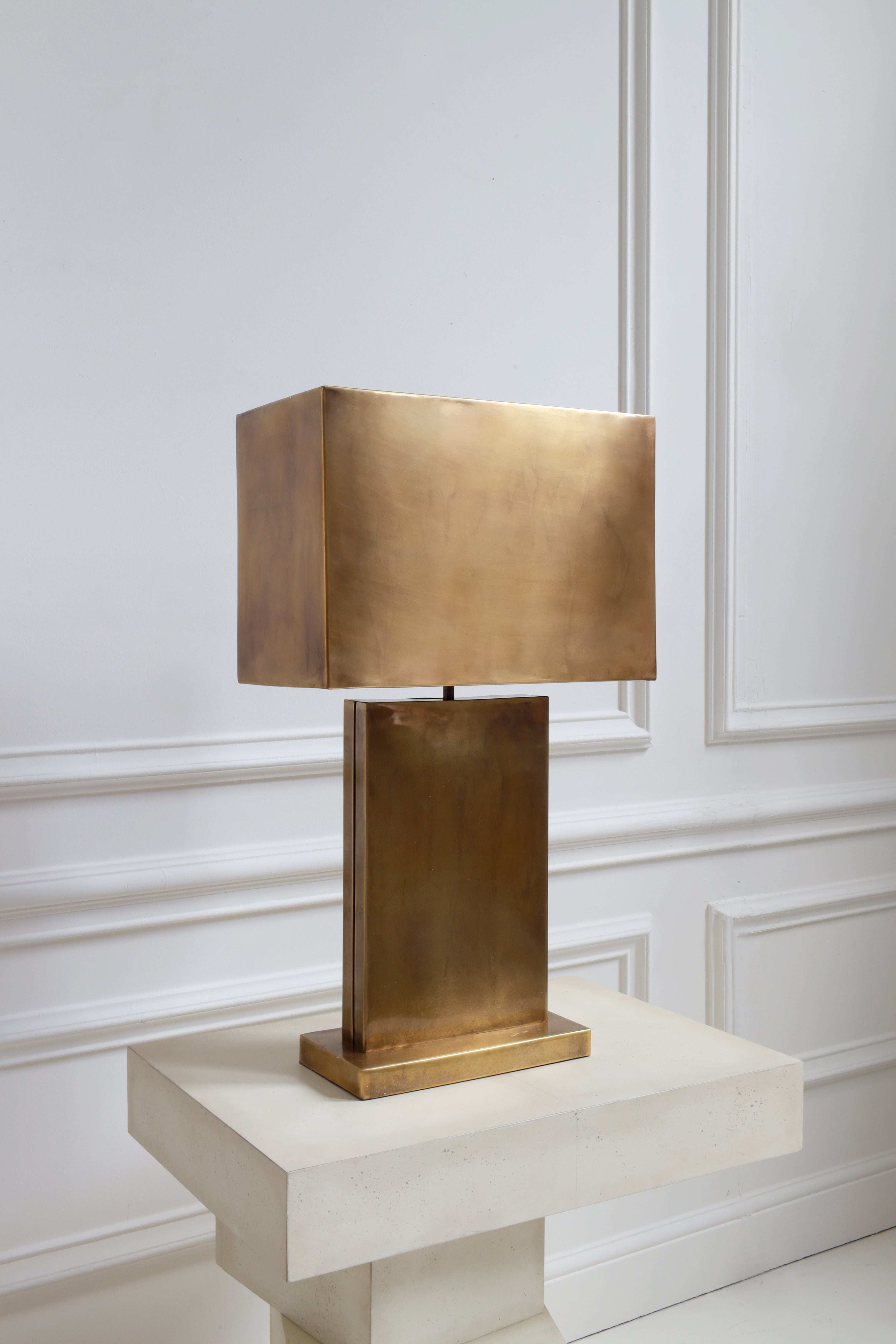 Gold table lamp on a white pedestal against a white wall with decorative molding.