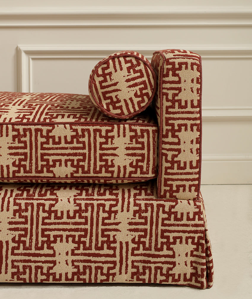 A close-up of an upholstered bench or sofa section with a round matching cushion, featuring a red and beige geometric pattern against a cream paneled wall.