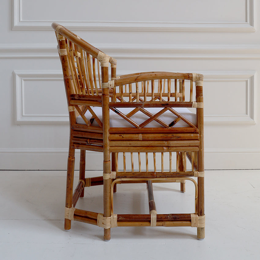 Rattan chair with a white cushion against a white paneled wall.