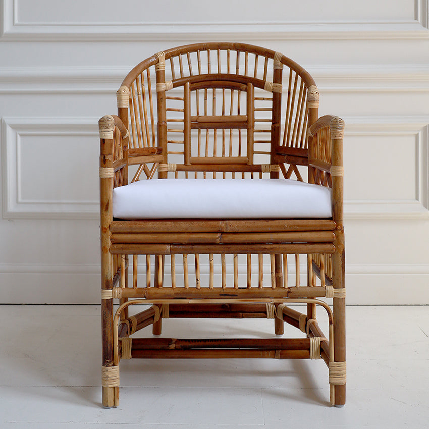 Rattan chair with a white cushion against a white paneled wall.