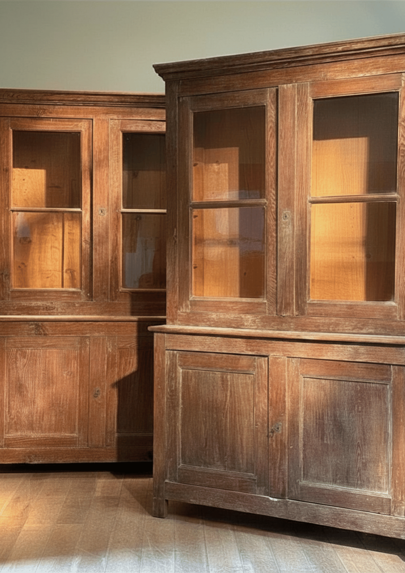 A rustic dark brown wooden hutch with glass-front upper cabinets and paneled lower cabinets, shown alongside a matching wooden cabinet in an indoor room setting.