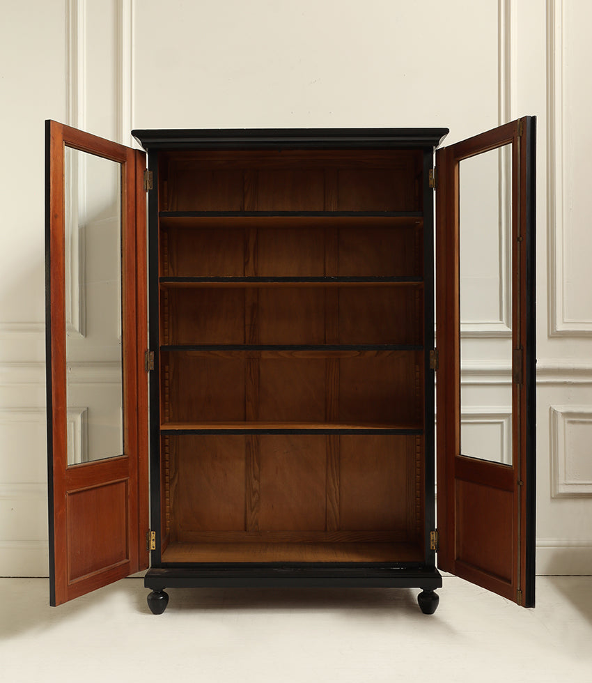 A tall wooden bookcase cabinet with two open doors, shown in a clean interior setting. The cabinet features a dark top and bottom frame with warm brown wood shelves and reddish-brown wooden door frames with glass panels.