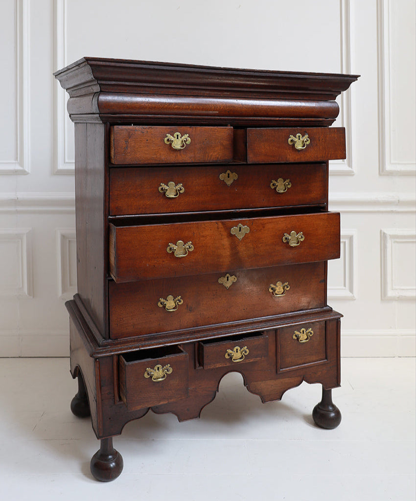 Wooden dresser with multiple drawers and brass handles against a white wall.