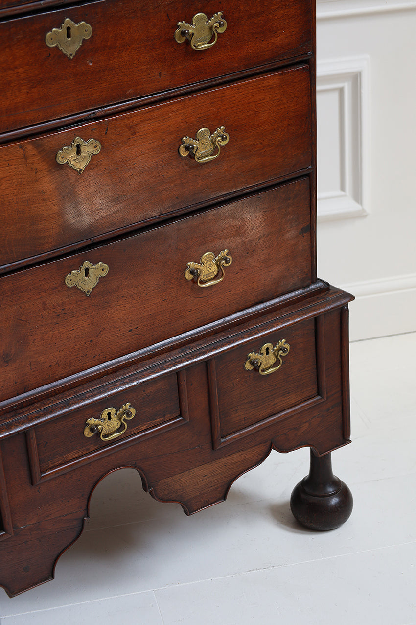 Wooden dresser with brass handles on a white floor and wall.