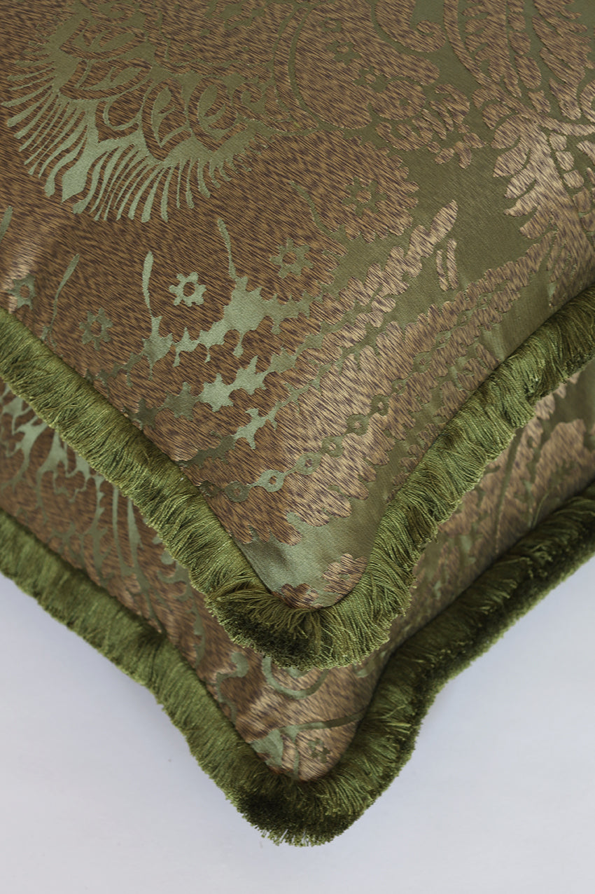 Close-up of a decorative throw pillow corner showing a metallic olive green and brown damask pattern with a fringed edge.