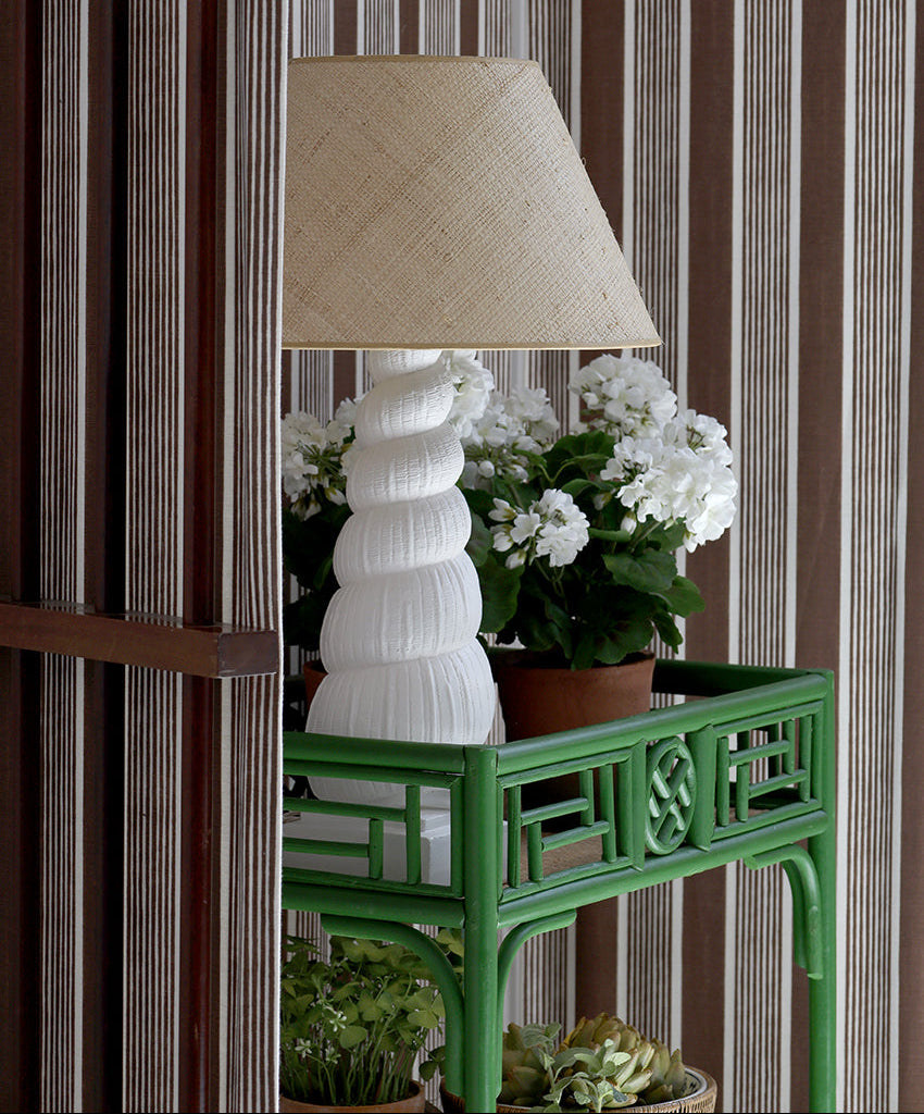 Green table with a white lamp and potted plants against striped wallpaper