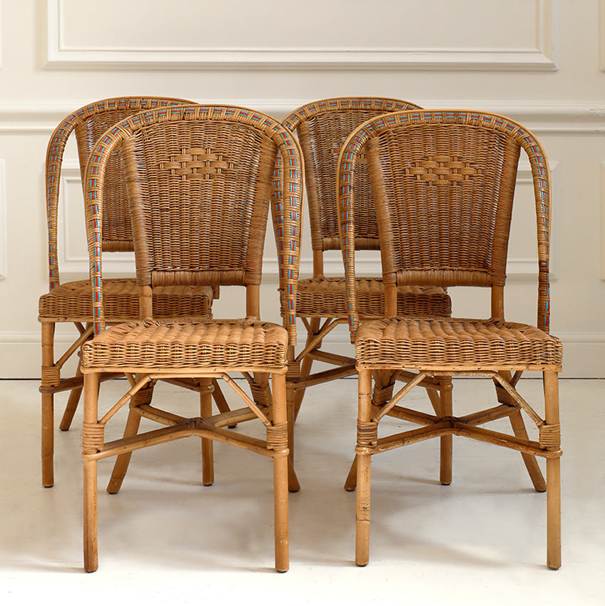 Four wicker chairs arranged in a row against a neutral wall.
