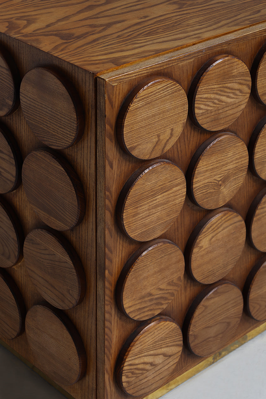 Close-up of a wooden side table or cabinet with a geometric design featuring circular wooden inserts on the front and side panels.