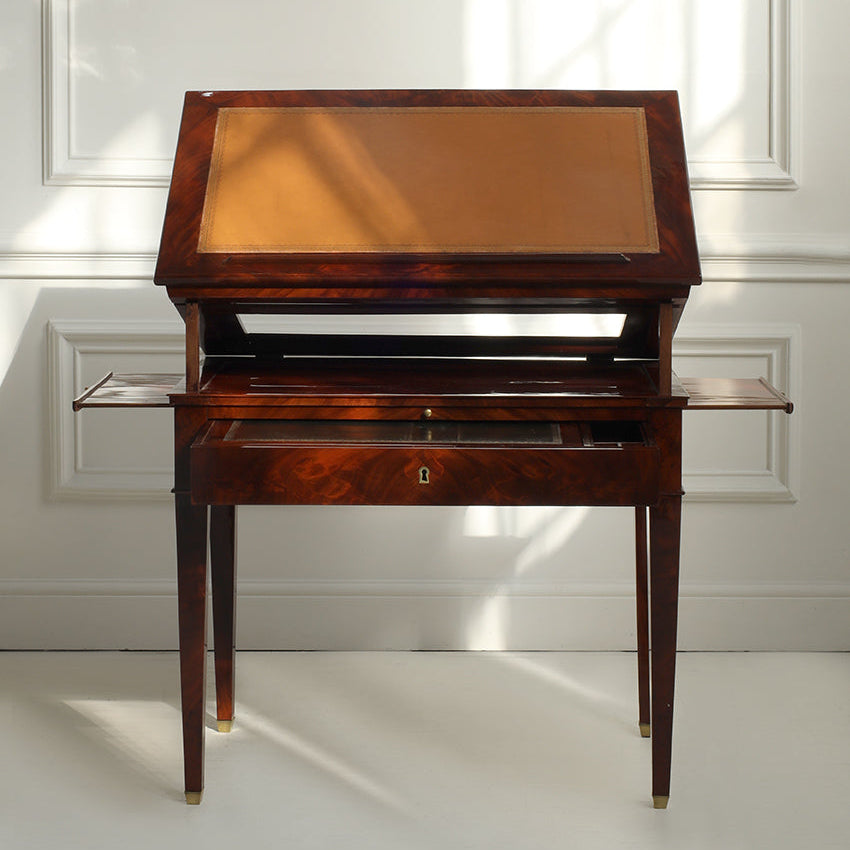Wooden desk with glass top in a room with sunlight streaming through a window.