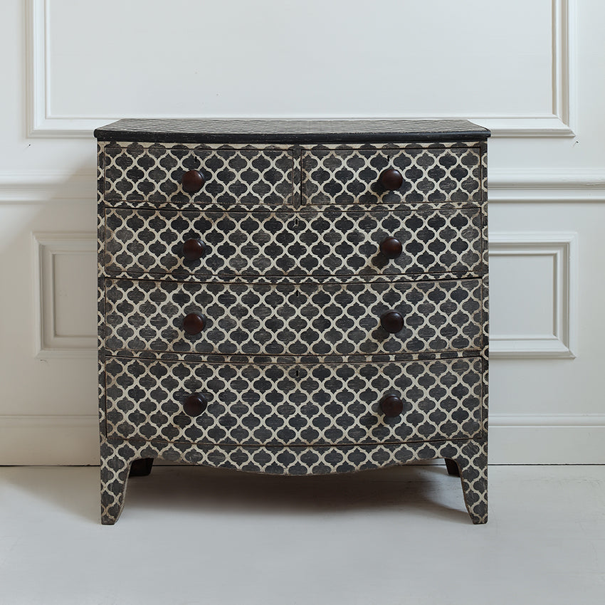 A vintage-style four-drawer chest of drawers with a black and white Moroccan trellis pattern and dark brown round knobs, set against a white paneled wall.