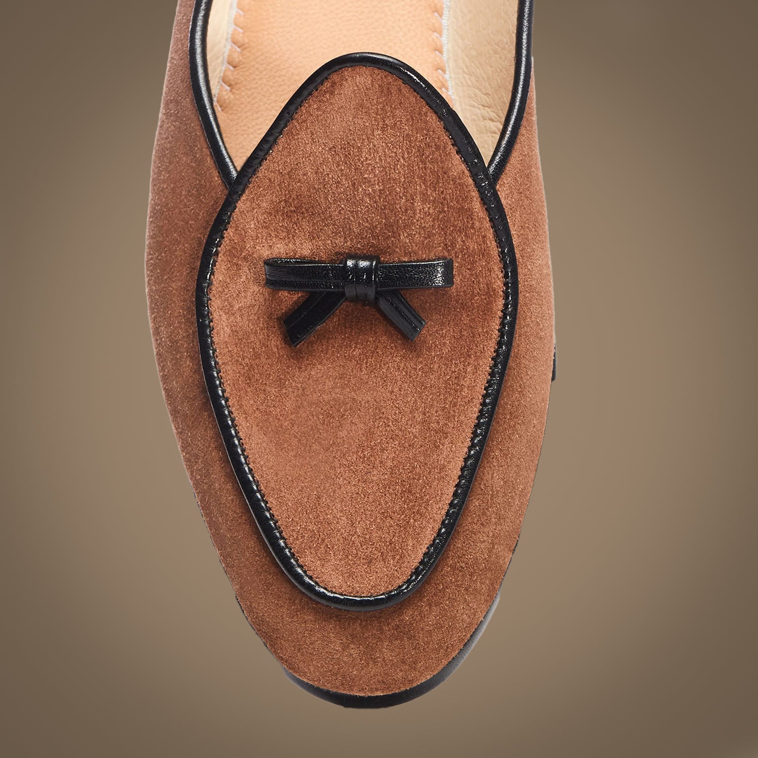 Brown suede loafer with a black bow on a beige background