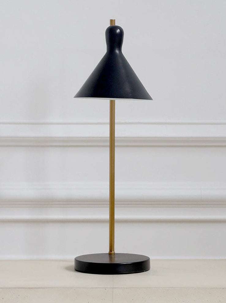 Black table lamp with a gold stem on a white surface against a light gray wall.