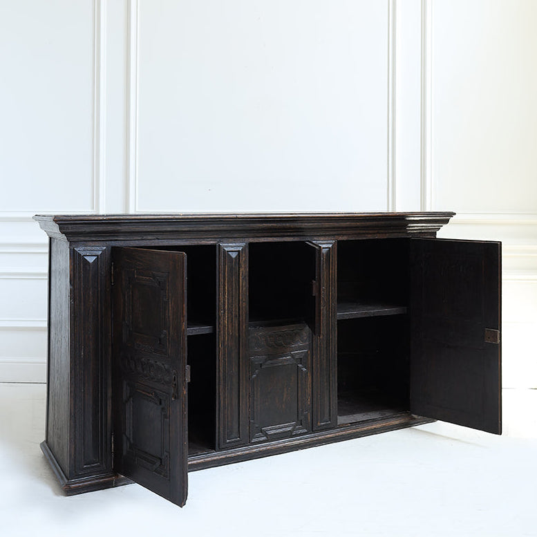 Dark wooden sideboard with open doors against a white paneled wall.