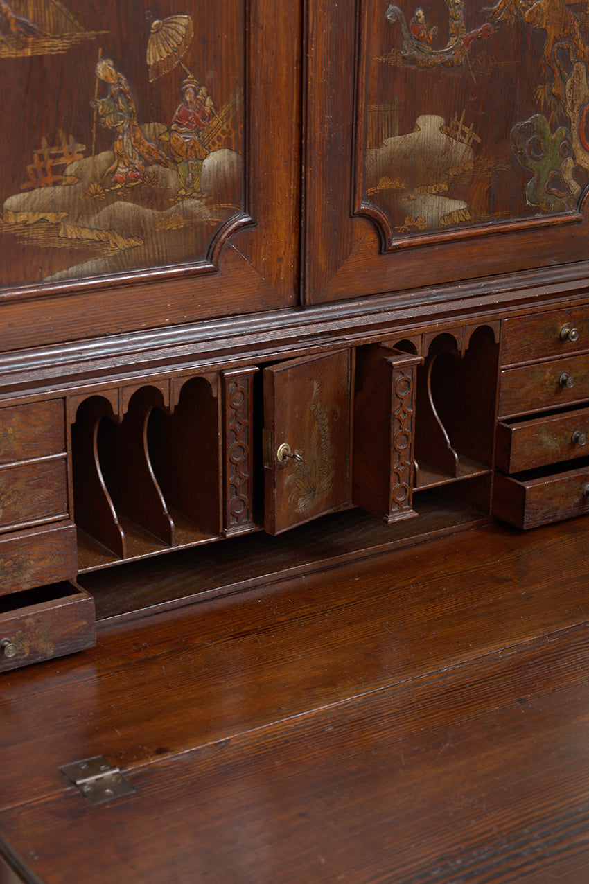 Close-up of a dark brown wooden writing desk with hand-painted lacquering on the cabinet doors and carved drawer compartments.