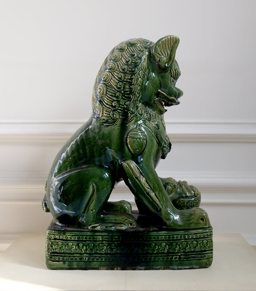 Green ceramic lion statue on a white surface with a white wall background