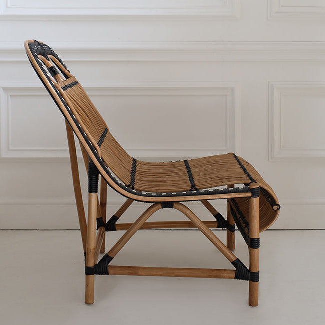 Handcrafted rattan chair with black straps against a white paneled wall.