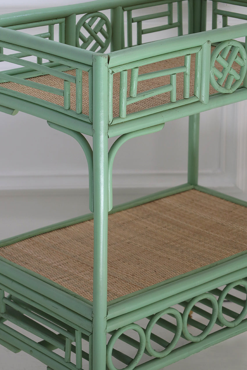 Green rattan bar cart with woven shelves on a white background