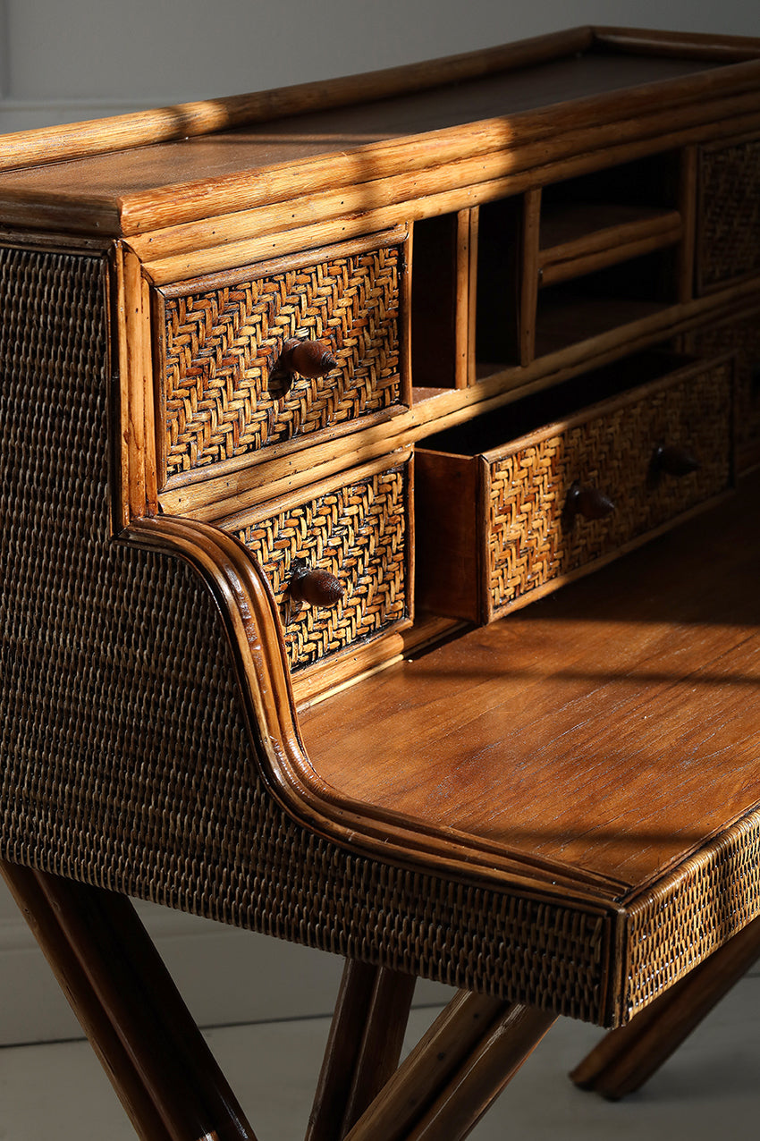 Wooden desk with wicker accents and drawers on a gray background