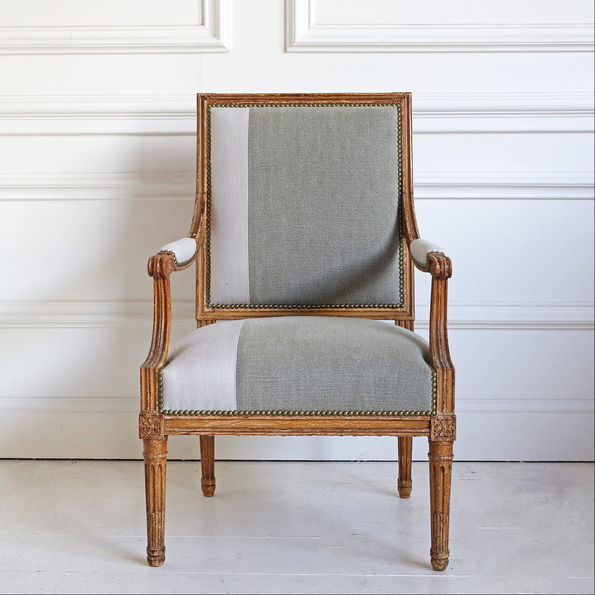 Vintage-style armchair with wooden frame and gray cushion against a white wall.