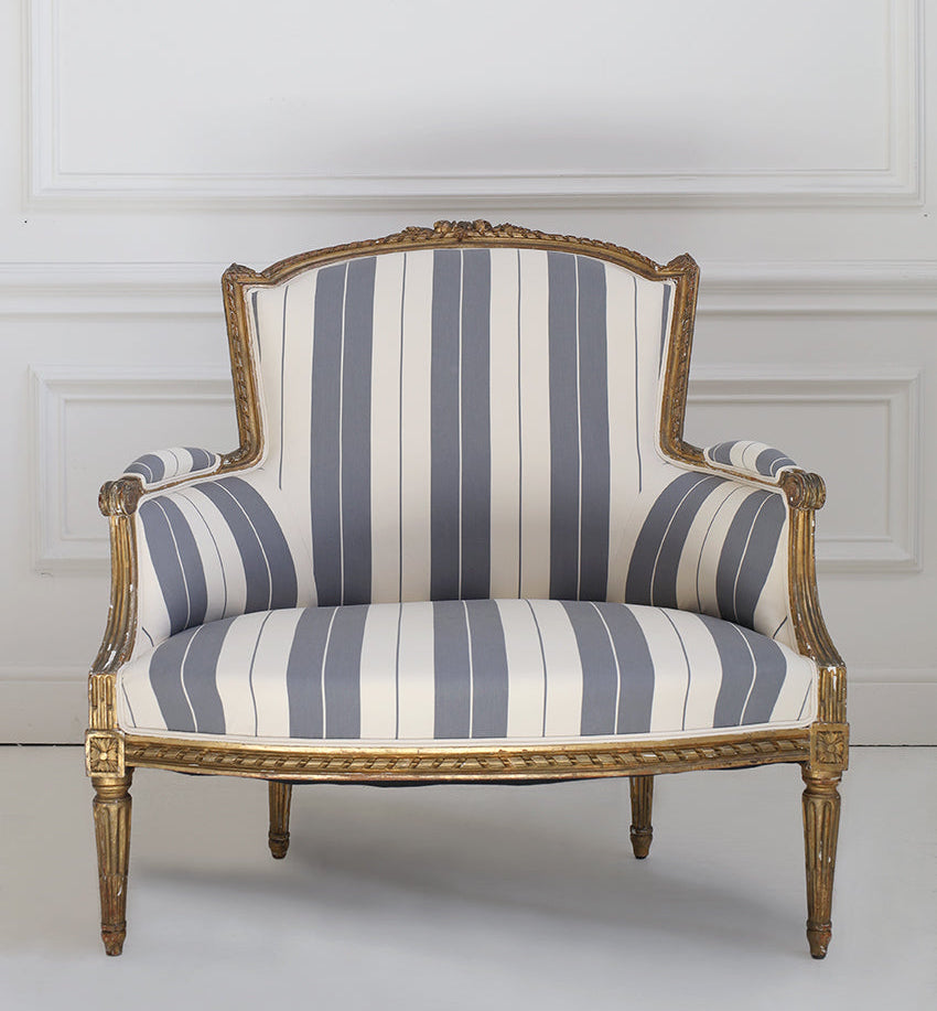 Striped armchair with gold frame against a white wall
