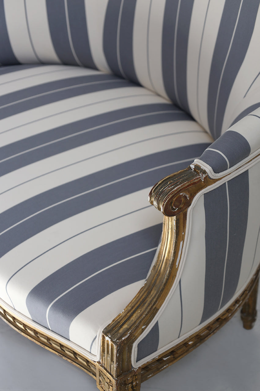 Chair with blue and white striped cushion and gold frame on a light gray background