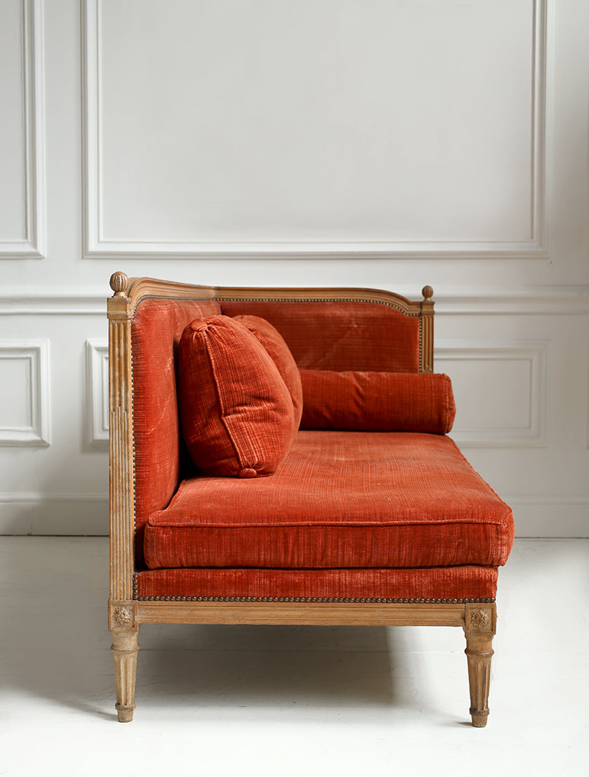 Orange velvet chaise lounge against a white paneled wall