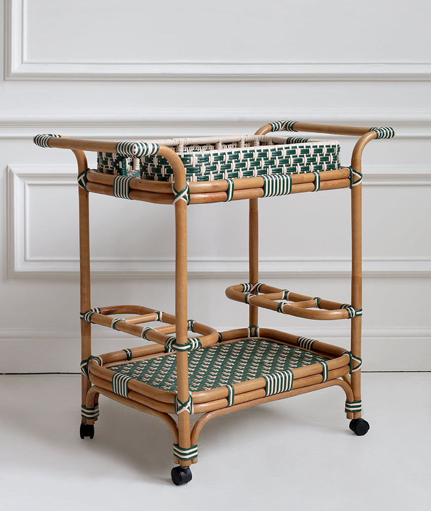 Rattan bar cart with woven top and bottom shelves against a white wall.