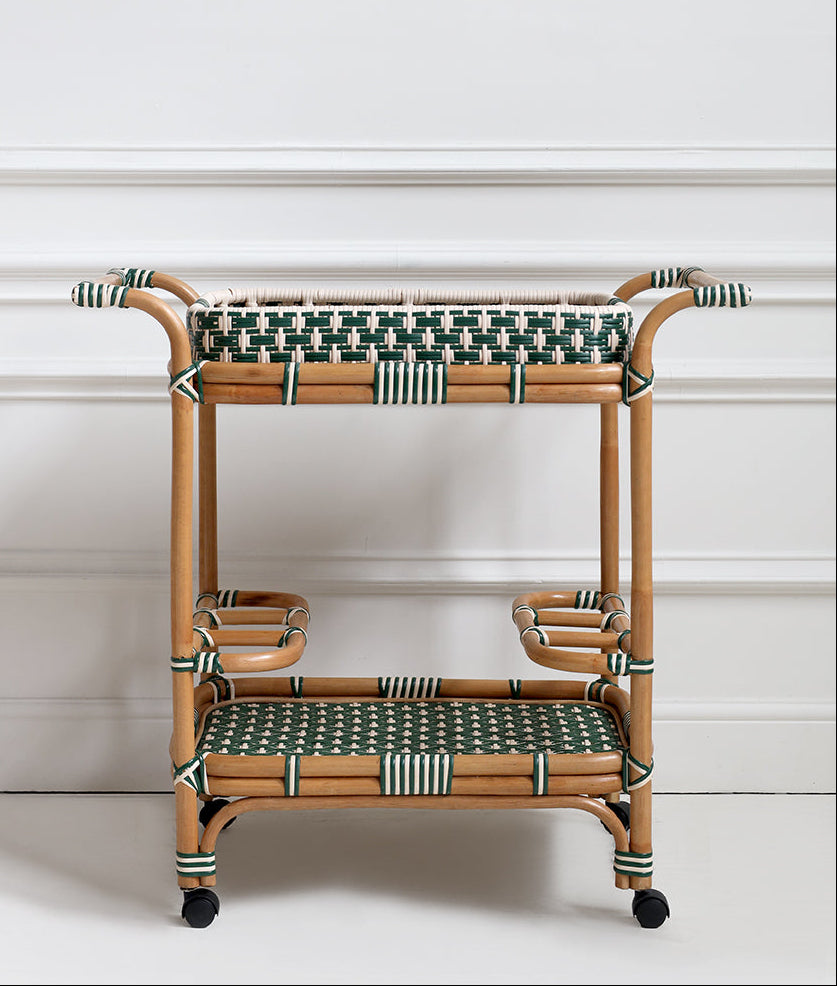 Rattan side table with green woven top and bottom shelves against a white wall.