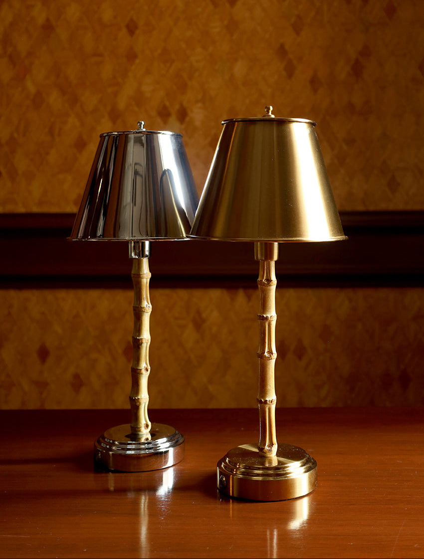 Two table lamps with metallic shades and bamboo-style bases, displayed on a wooden table against a patterned brown wall.