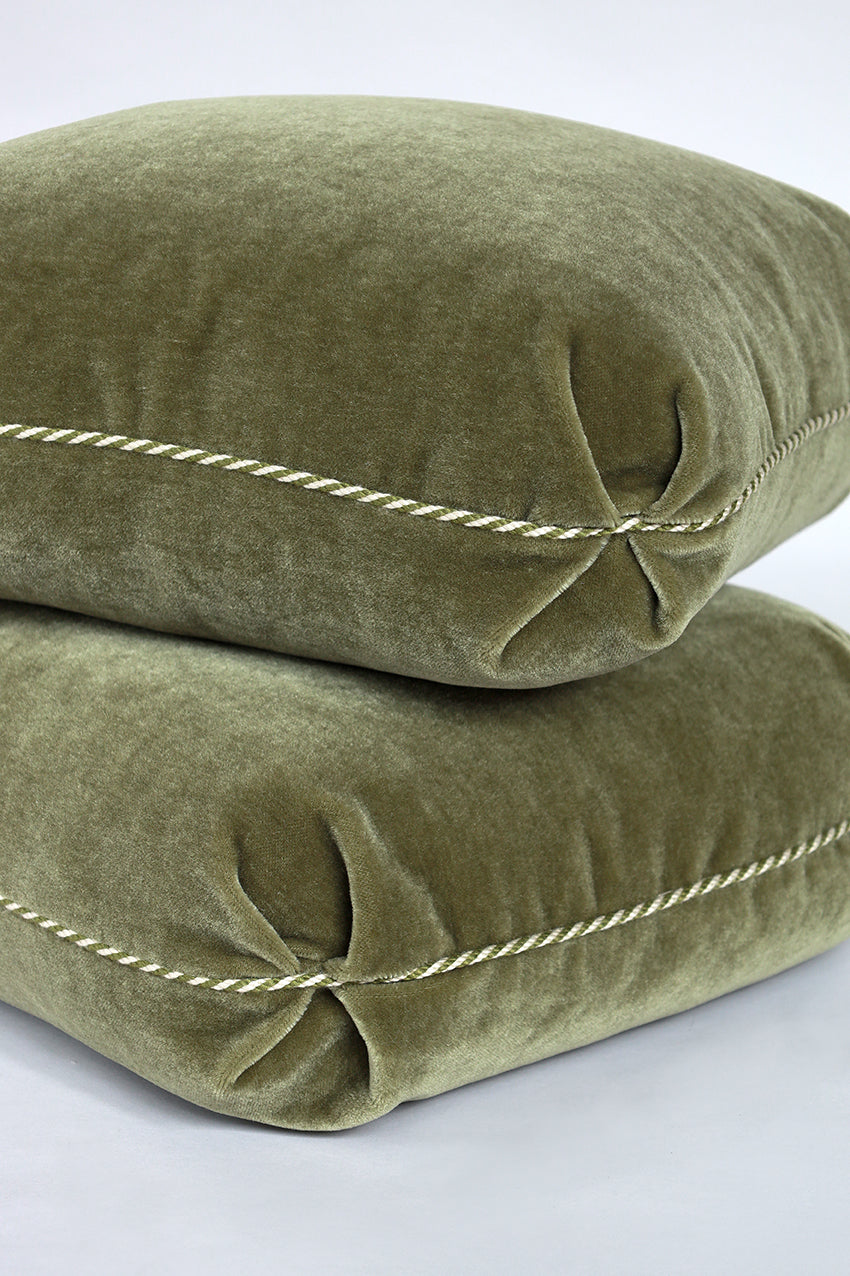 Two green velvet pillows with decorative stitching on a white background