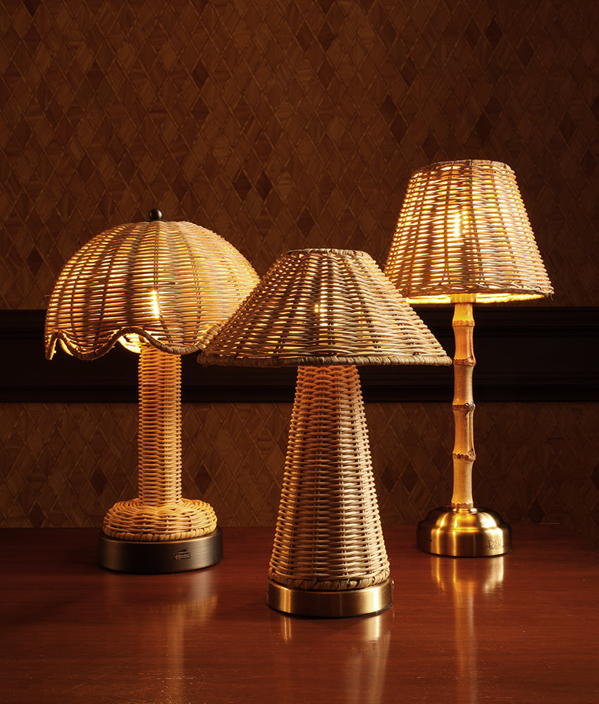 Three woven rattan table lamps with warm glowing bulbs, displayed on a polished wooden table against a textured brown wall.