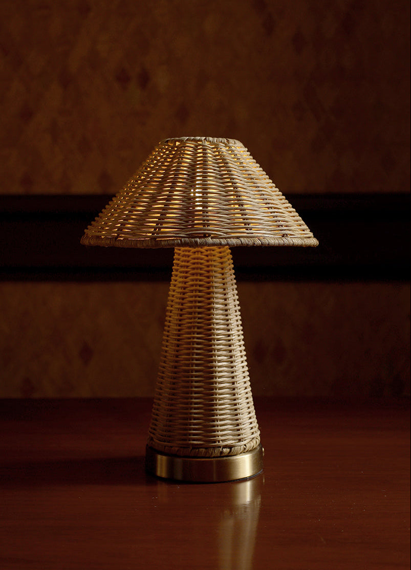 A small table lamp with a woven natural-fiber shade and matching textured base, sitting on a dark wooden surface against a dimly lit patterned wall.