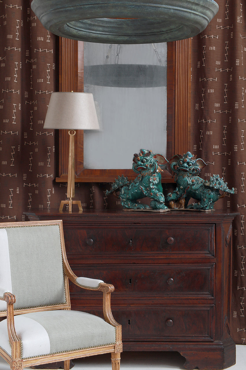 Wooden dresser with decorative items, mirror, and chair in a room with patterned wallpaper.