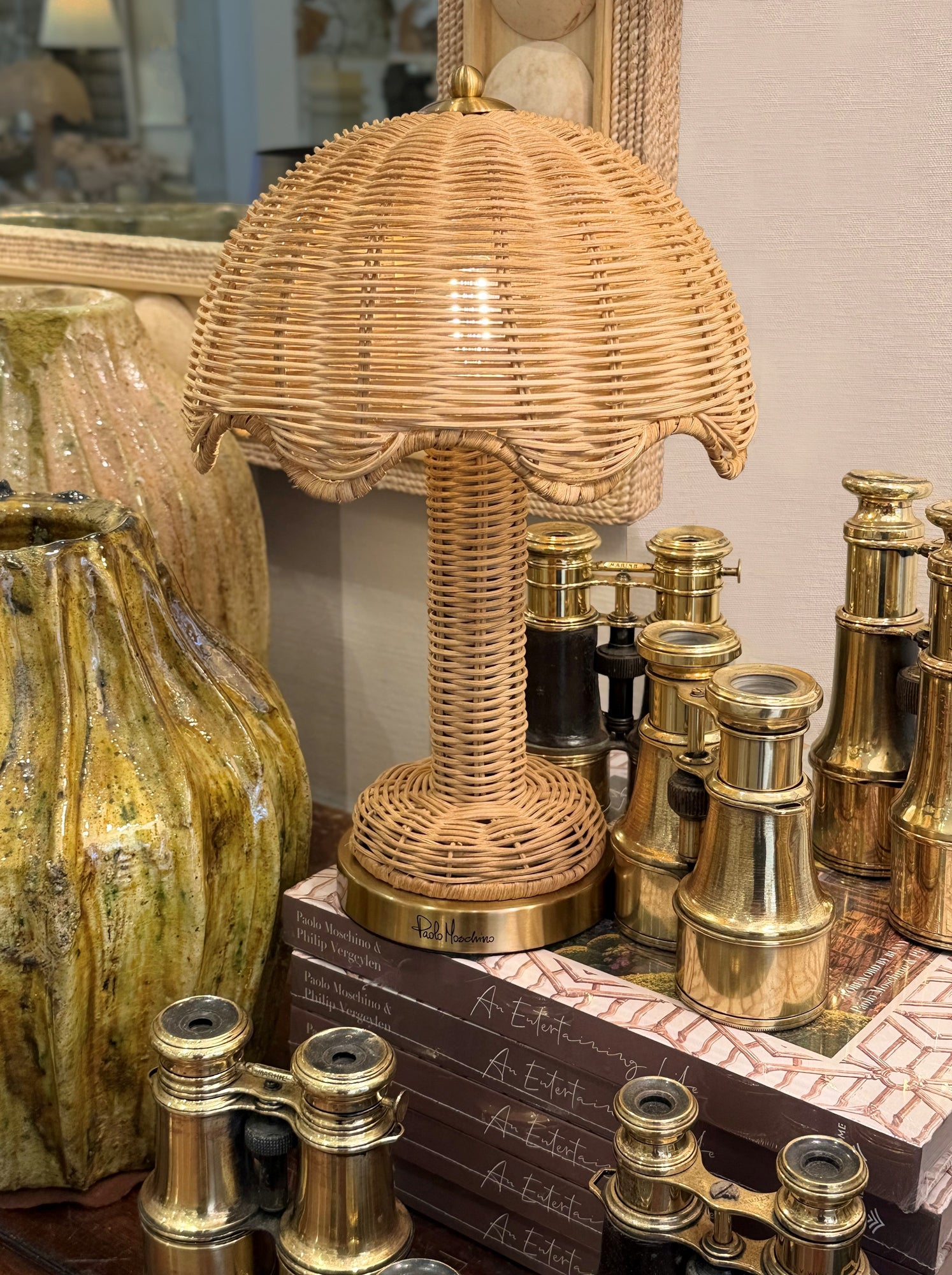 Wicker lamp with wicker shade on a surface with vintage binoculars and books.